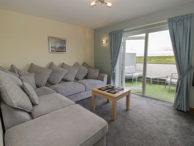 A living room with a gray sectional sofa a wooden coffee table and sliding glass doors leading to an outdoor seating area at Sea Spray in Dinas Dinlle