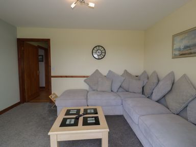 A living room with a grey corner sofa and a wooden coffee table with a remote control on it at Sea Spray in Dinas Dinlle