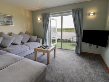 A living room with a sofa set coffee table TV and sliding door leading to a balcony at Sea Spray in Dinas Dinlle