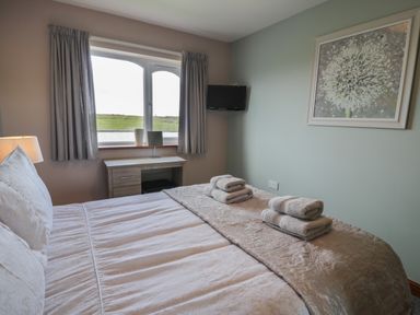 A bedroom with a bed with folded towels on it a window a desk a wall-mounted TV and a framed picture at Sea Spray in Dinas Dinlle