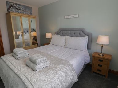 A bedroom with a bed with folded towels bedside tables with lamps and a wardrobe with mirrored doors at Sea Spray in Dinas Dinlle