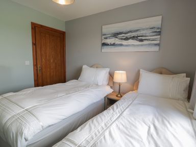 A bedroom with two single beds a lamp on a bedside table and a painting above the beds at Sea Spray in Dinas Dinlle