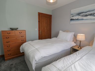 A bedroom with two single beds a wooden chest of drawers a bedside table with a lamp and a painting on the wall at Sea Spray in Dinas Dinlle
