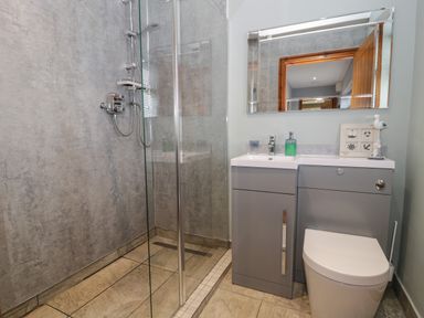A bathroom with a glass shower enclosure a gray vanity unit with a sink and a toilet at Sea Spray in Dinas Dinlle