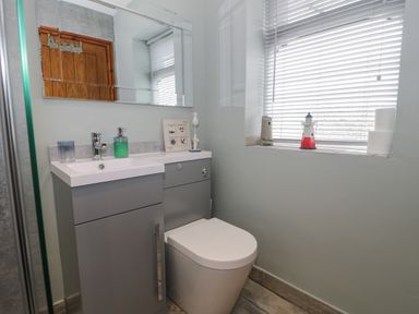 A bathroom with a toilet sink cabinet and window with blinds at Sea Spray in Dinas Dinlle