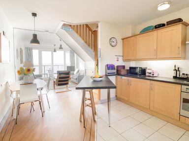 A kitchen with wooden cabinets and a dining area with a table and chairs at 12 West End Point in Pwllheli