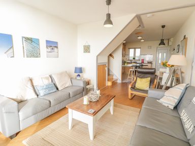 A living room with two gray sofas a wooden coffee table and an armchair next to an open kitchen at 12 West End Point in Pwllheli