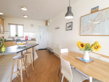 A kitchen and dining area with wooden stools at a counter and a table with sunflowers in a vase at 12 West End Point in Pwllheli
