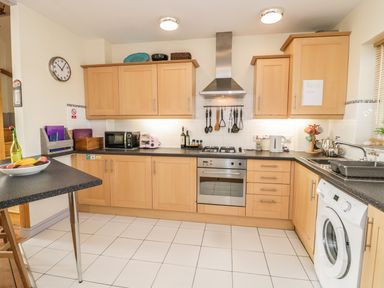 A kitchen with wooden cabinets a gas stove an oven a washing machine and a countertop with various appliances at 12 West End Point in Pwllheli