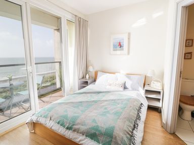 A bedroom with a double bed a balcony overlooking the sea and an ensuite bathroom at 12 West End Point in Pwllheli