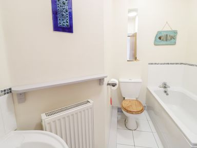 A bathroom with a toilet with wooden seat a bathtub a radiator and wall decorations at 12 West End Point Pwllheli