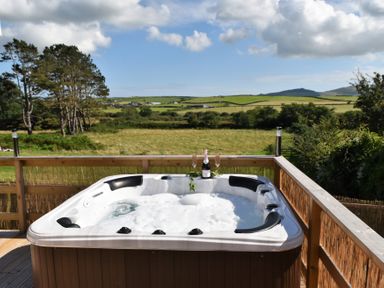 A hot tub on a wooden deck overlooking fields at Y Caban Clyd in Morfa Nefyn