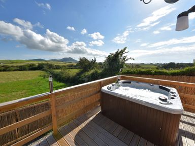 An outdoor hot tub on a wooden deck with countryside hills and fields in the background at Y Caban Clyd in Morfa Nefyn