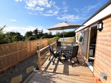 An outdoor wooden deck with a round black table and four chairs under a large umbrella at Y Caban Clyd in Morfa Nefyn