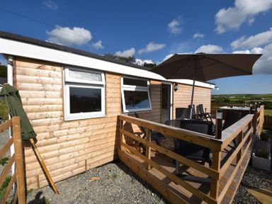 A wooden cabin with a deck patio featuring table chairs and a large umbrella at Y Caban Clyd in Morfa Nefyn