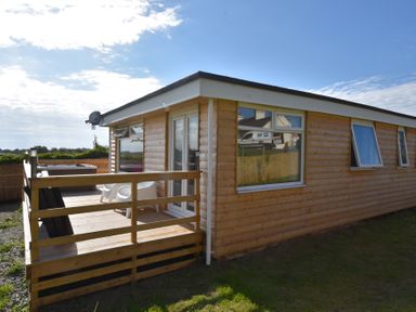 A wooden cabin with a small deck and white chairs under a blue sky at Y Caban Clyd in Morfa Nefyn