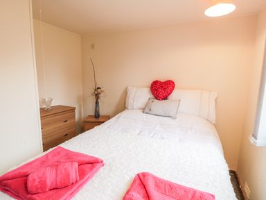 A bedroom with a double bed with white bedding and red towels on the bed at Y Caban Clyd in Morfa Nefyn