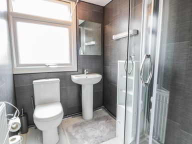 A small bathroom with a toilet sink mirror shower and shelving unit at Y Caban Clyd in Morfa Nefyn