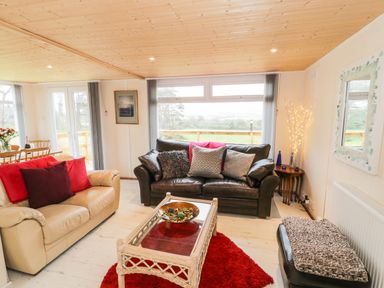 A living room with two sofas cushions a glass coffee table and a dining table with flowers at Y Caban Clyd in Morfa Nefyn