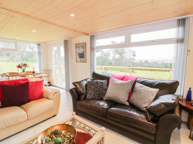 A living room with two sofas a coffee table and a dining table near large windows at Y Caban Clyd in Morfa Nefyn