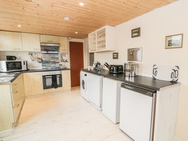 A kitchen with wooden cabinets white appliances black countertops and wooden ceiling at Y Caban Clyd in Morfa Nefyn