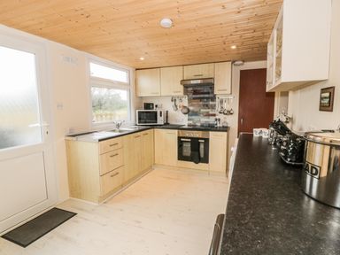 A kitchen with wooden cabinets a stove microwave and black countertop at Y Caban Clyd in Morfa Nefyn