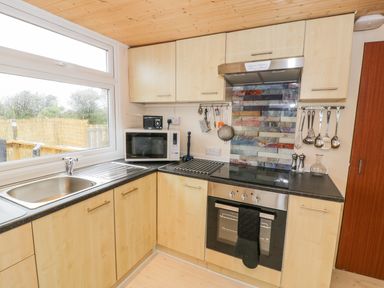 A kitchen with wooden cabinets a stainless steel sink microwave oven stovetop and kitchen utensils at Y Caban Clyd in Morfa Nefyn
