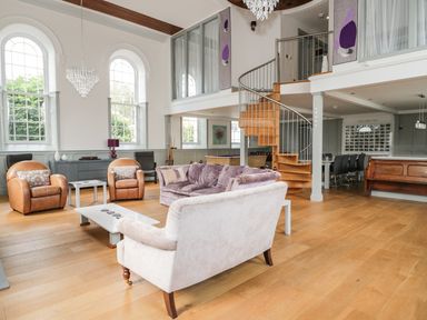 A living room with sofas chairs a spiral staircase and large arched windows at Capel Bryn Bachau in Chwilog near Criccieth
