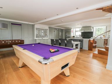 A room with a pool table with purple felt a dining table with chairs a kitchen area and a spiral staircase at Capel Bryn Bachau in Chwilog near Criccieth