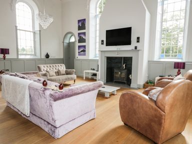 A living room with sofas a fireplace a television and large arched windows at Capel Bryn Bachau in Chwilog near Criccieth