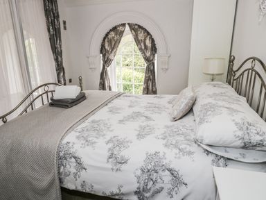 A bedroom with a metal bed frame patterned bedding folded towels and curtains at Capel Bryn Bachau in Chwilog near Criccieth