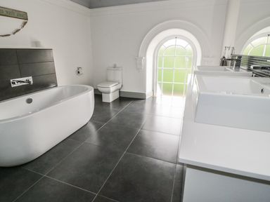 A bathroom with a bathtub toilet double sinks and an arched window at Capel Bryn Bachau in Chwilog near Criccieth
