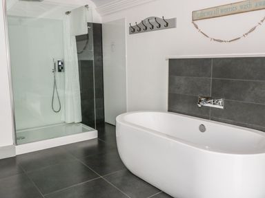 A bathroom with a freestanding bathtub and a glass-enclosed shower with a curtain at Capel Bryn Bachau Chwilog near Criccieth