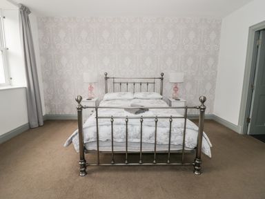 A bedroom with a metal bed frame two bedside tables with lamps and a window with curtains at Capel Bryn Bachau in Chwilog near Criccieth
