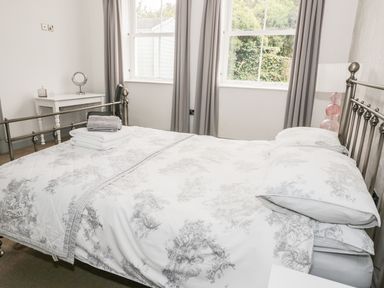 A bedroom with a bed with patterned bedding two windows with curtains a desk with a mirror and a chair at Capel Bryn Bachau Chwilog near Criccieth