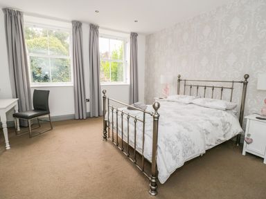 A bedroom with a metal bed frame a desk with a chair two windows and bedside tables at Capel Bryn Bachau in Chwilog near Criccieth