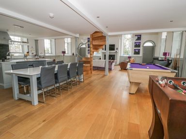 An open plan room with a dining table and chairs a kitchen a wooden spiral staircase a pool table a foosball table and seating area at Capel Bryn Bachau in Chwilog near Criccieth