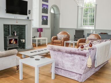 A living room with a fireplace a mounted tv brown leather armchairs and a purple sofa at Capel Bryn Bachau in Chwilog near Criccieth