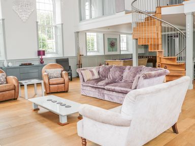 A living room with sofas, armchairs, a coffee table, spiral staircase, and windows at Capel Bryn Bachau in Chwilog near Criccieth