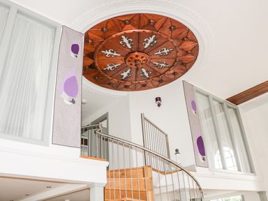 A spiral wooden staircase with metal railing under a round decorative wooden ceiling panel in a white room at Capel Bryn Bachau in Chwilog near Criccieth