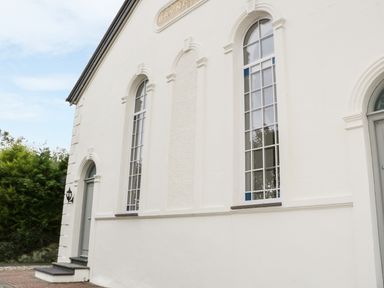 Exterior view of a white building with tall arched windows and a gray door at Capel Bryn Bachau in Chwilog near Criccieth
