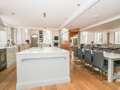 An open kitchen and dining area with a white island countertop black chairs spiral staircase and windows at Capel Bryn Bachau in Chwilog near Criccieth