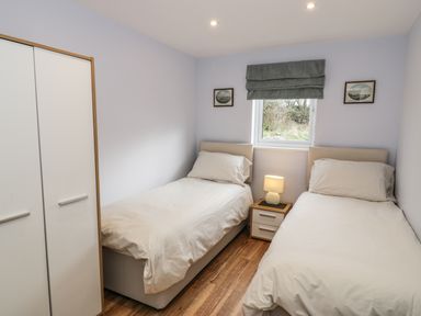 A bedroom with two single beds a nightstand with a lamp a window and a wardrobe at Nant Y Felin Lodge in Aberdaron