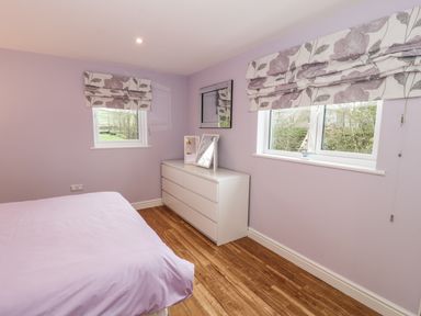 A bedroom with a purple bedspread two windows with floral blinds a white dresser and a mirror at Nant Y Felin Lodge in Aberdaron