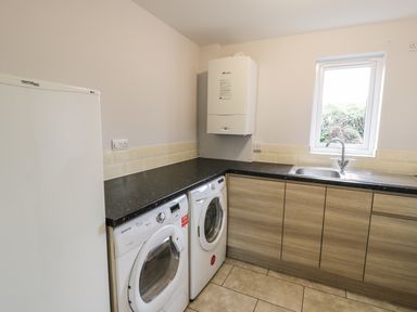 A utility room with a washing machine dryer refrigerator sink countertop and cabinets at Nant Y Felin Lodge in Aberdaron