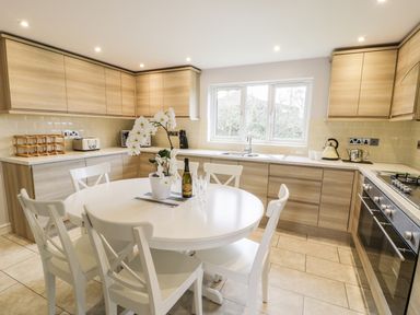 A kitchen with wooden cabinets a white round table with chairs and kitchen appliances at Nant Y Felin Lodge in Aberdaron