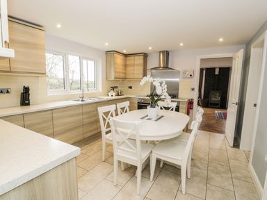A kitchen with wooden cabinets a white dining table and chairs and a potted plant on the table at Nant Y Felin Lodge in Aberdaron