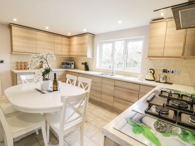 A kitchen with wooden cabinets a white dining table with chairs and a stove at Nant Y Felin Lodge Aberdaron