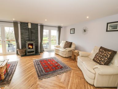 A living room with two cream leather sofas a fireplace rugs and glass doors leading outside at Nant Y Felin Lodge in Aberdaron