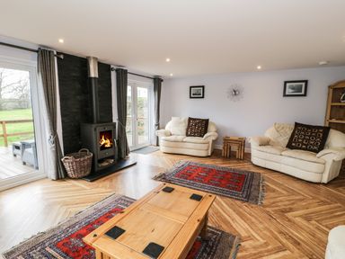 A living room with two cream sofas a wooden coffee table a wood burning stove and two red rugs at Nant Y Felin Lodge in Aberdaron